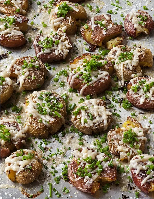Ina Garten Parmesan chive smashed potatoes on a sheet pan topped with melted cheese and minced chives