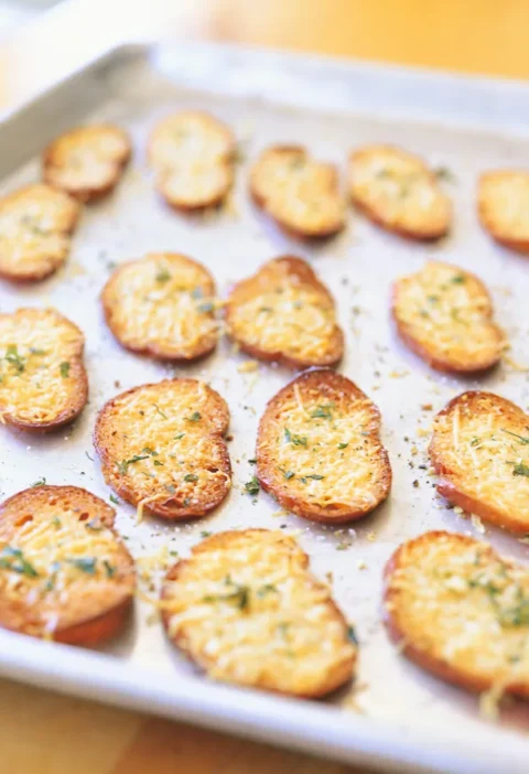 Ina Garten parmesan croutons, golden baguette slices topped with melted shredded Parmesan and herbs on a baking sheet