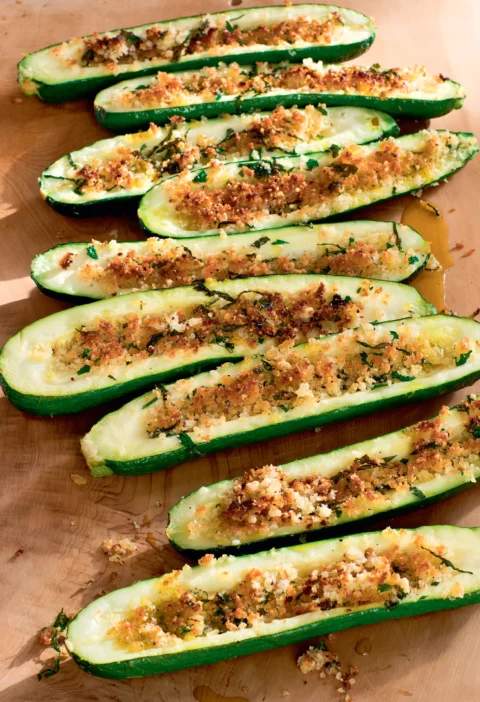 Ina Garten parmesan roasted zucchini halves topped with golden panko, herbs and garlic on a wooden board