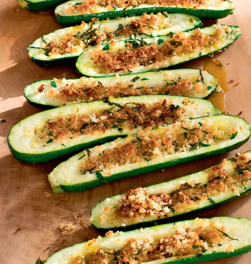 Ina Garten parmesan roasted zucchini halves topped with golden panko, herbs and garlic on a wooden board