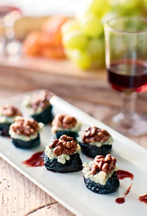 Ina Garten port wine prunes with stilton and walnuts on a white platter with a glass of red wine