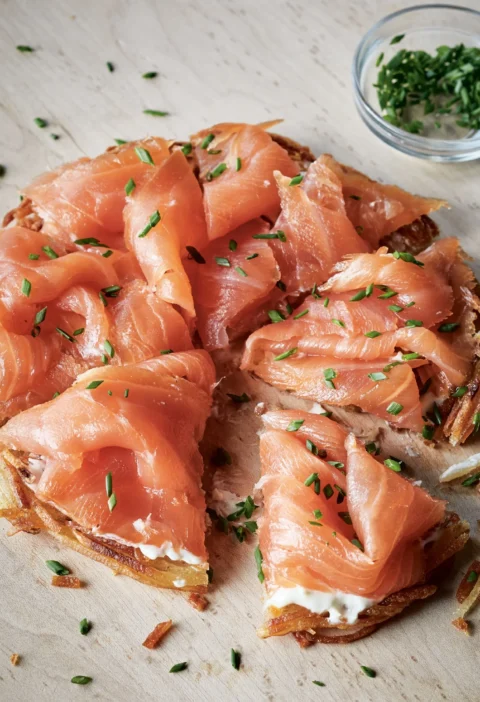 Ina Garten potato galettes with smoked salmon, crème fraîche and minced chives on a wooden cutting board