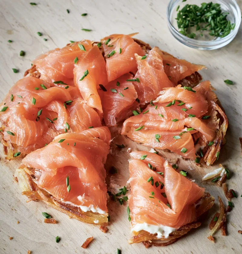 Ina Garten potato galettes with smoked salmon, crème fraîche and minced chives on a wooden cutting board