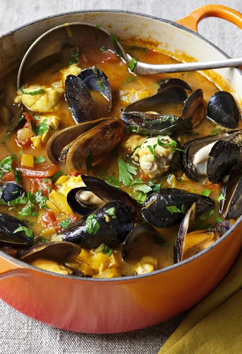 Ina Garten Provençal fish stew with Sriracha rouille in an orange Dutch oven with mussels, cod, tomatoes and parsley