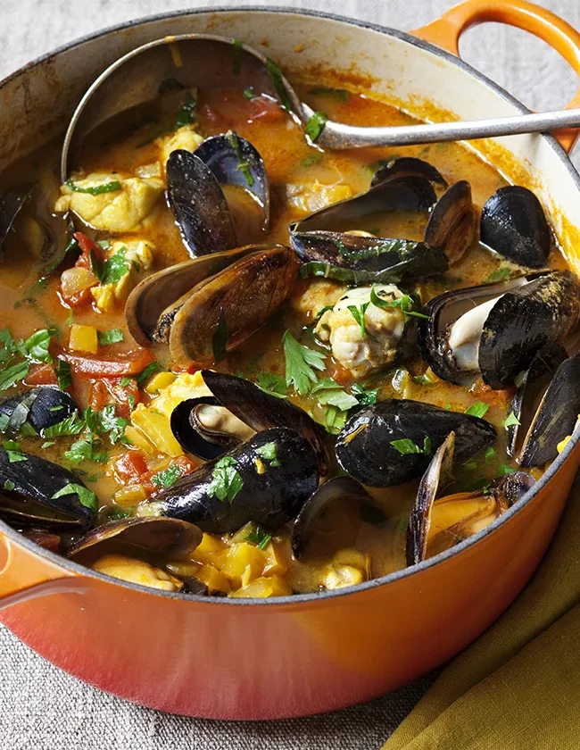 Ina Garten Provençal fish stew with Sriracha rouille in an orange Dutch oven with mussels, cod, tomatoes and parsley