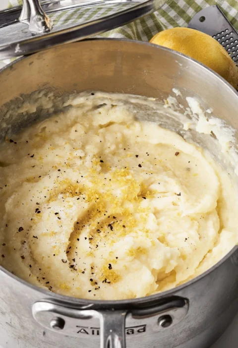 Ina Garten puréed potatoes with lemon in a saucepan, topped with lemon zest and black pepper, with a lemon and grater beside it