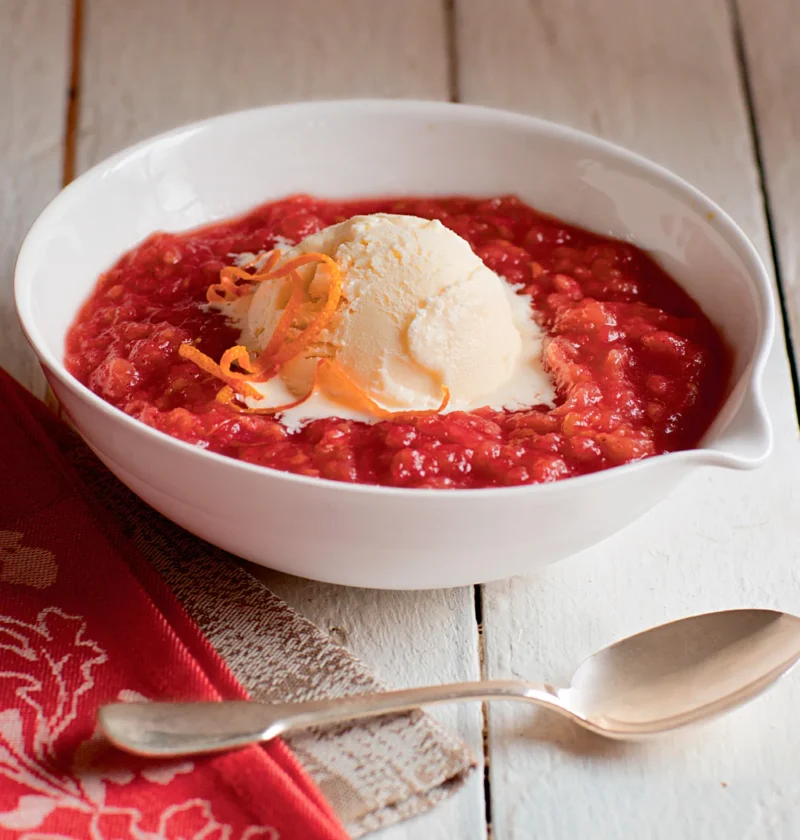 Ina Garten raspberry roasted applesauce in a white bowl topped with a scoop of vanilla ice cream and orange zest