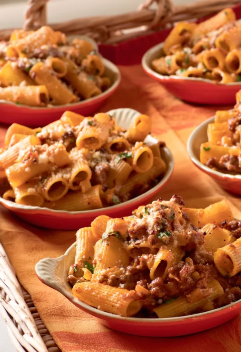 Ina Garten rigatoni with sausage and fennel in shallow red bowls topped with Parmesan and parsley