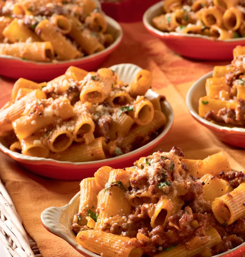 Ina Garten rigatoni with sausage and fennel in shallow red bowls topped with Parmesan and parsley