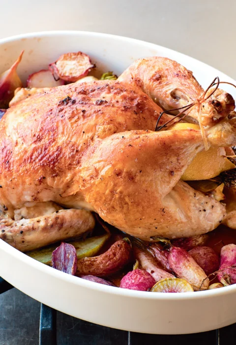 Ina Garten roast chicken with radishes, golden whole chicken with lemon and roasted heirloom radishes in a white baking dish
