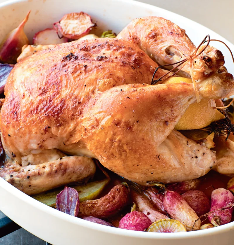 Ina Garten roast chicken with radishes, golden whole chicken with lemon and roasted heirloom radishes in a white baking dish