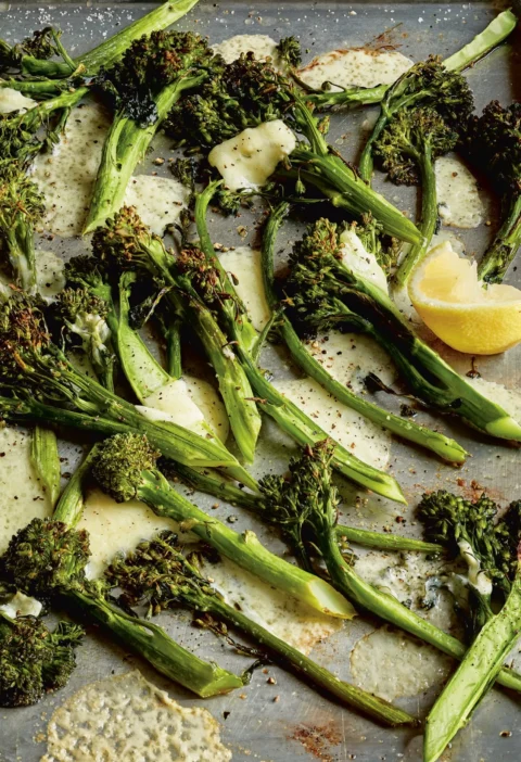 Ina Garten roasted broccolini & cheddar on a sheet pan with melted crispy Cheddar and a lemon wedge