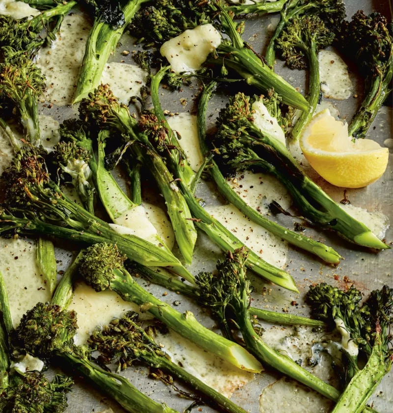 Ina Garten roasted broccolini & cheddar on a sheet pan with melted crispy Cheddar and a lemon wedge
