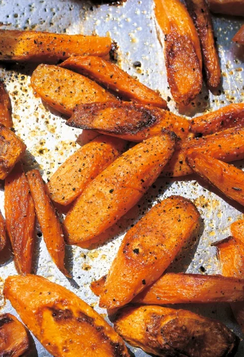 Ina Garten roasted carrots, caramelized diagonal slices with black pepper on a baking sheet