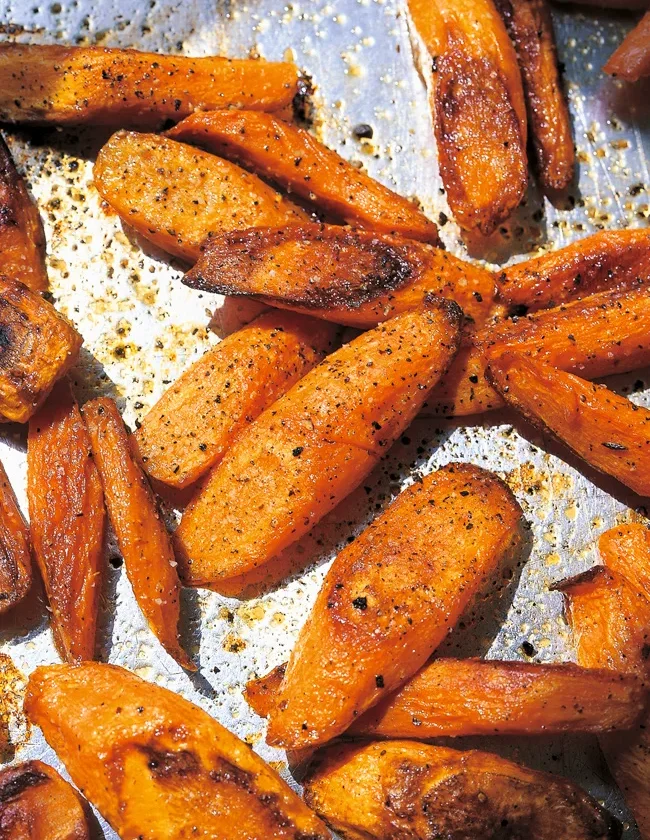 Ina Garten roasted carrots, caramelized diagonal slices with black pepper on a baking sheet