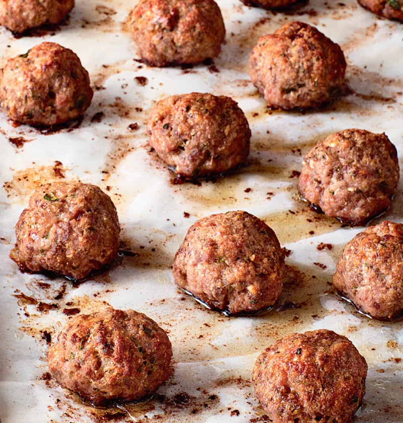 Ina Garten roasted Italian meatballs browned on a parchment-lined sheet pan