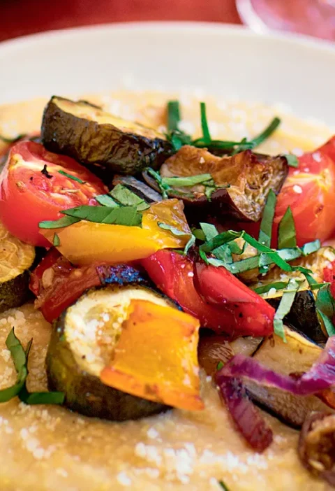 Ina Garten roasted ratatouille with polenta, showing roasted zucchini, eggplant, peppers and tomatoes topped with fresh basil over creamy polenta