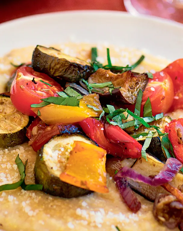 Ina Garten roasted ratatouille with polenta, showing roasted zucchini, eggplant, peppers and tomatoes topped with fresh basil over creamy polenta