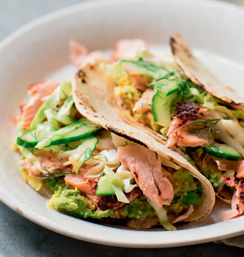 Ina Garten roasted salmon tacos with avocado, cucumber and cabbage slaw with dill in corn tortillas on a white plate