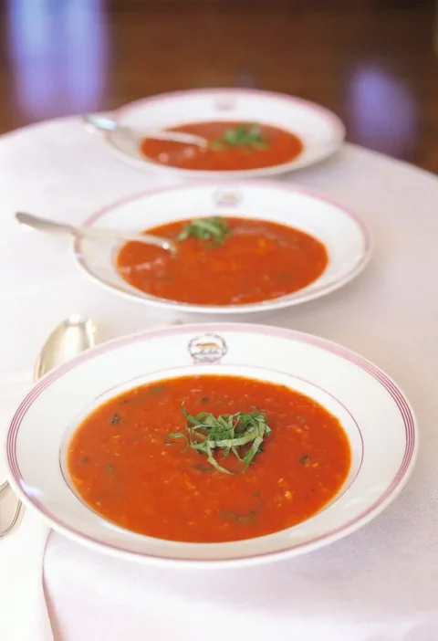Three white bowls of Ina Garten roasted-tomato basil soup topped with shredded fresh basil on a white tablecloth