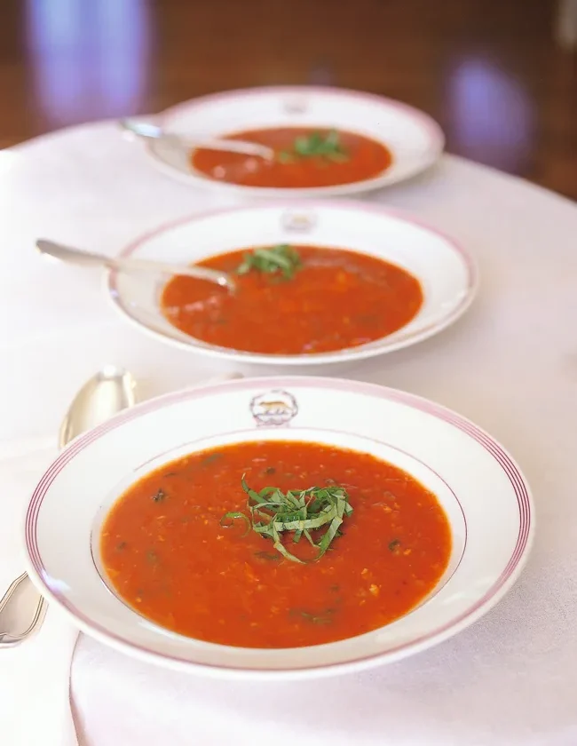 Three white bowls of Ina Garten roasted-tomato basil soup topped with shredded fresh basil on a white tablecloth