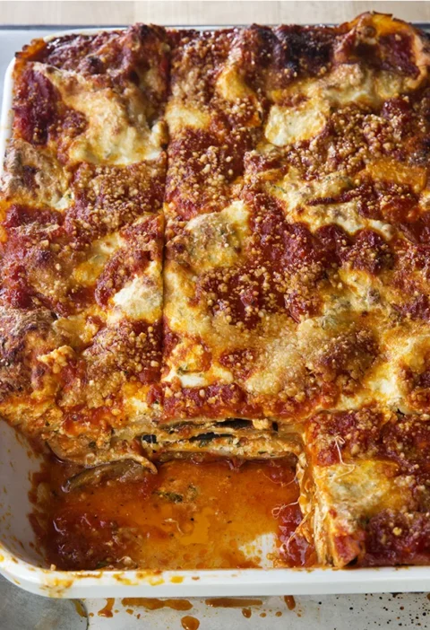 Ina Garten roasted vegetable lasagna in a white baking dish with browned Parmesan top and marinara, one square cut out to show the layers