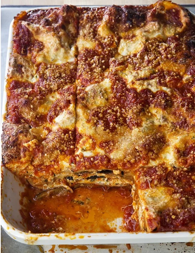 Ina Garten roasted vegetable lasagna in a white baking dish with browned Parmesan top and marinara, one square cut out to show the layers