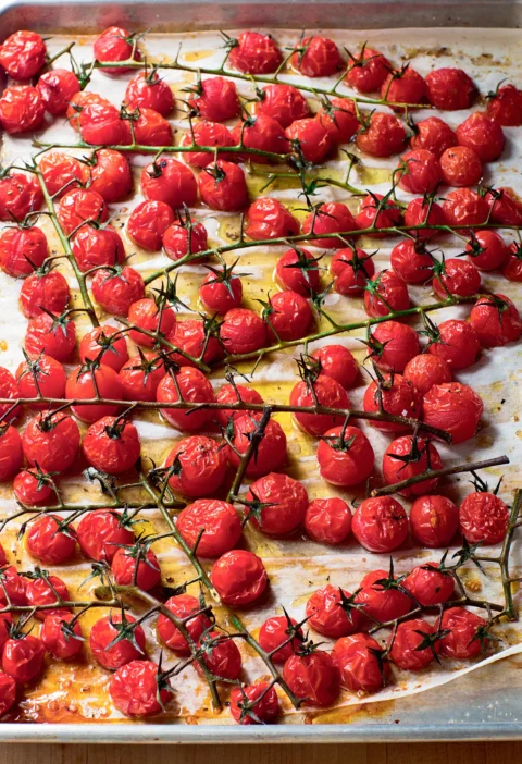 Ina Garten roasted vine tomatoes on a sheet pan lined with parchment, glossy and blistered with the green stems still attached
