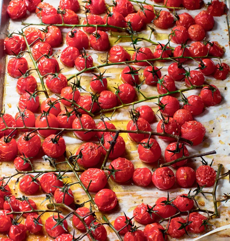 Ina Garten roasted vine tomatoes on a sheet pan lined with parchment, glossy and blistered with the green stems still attached