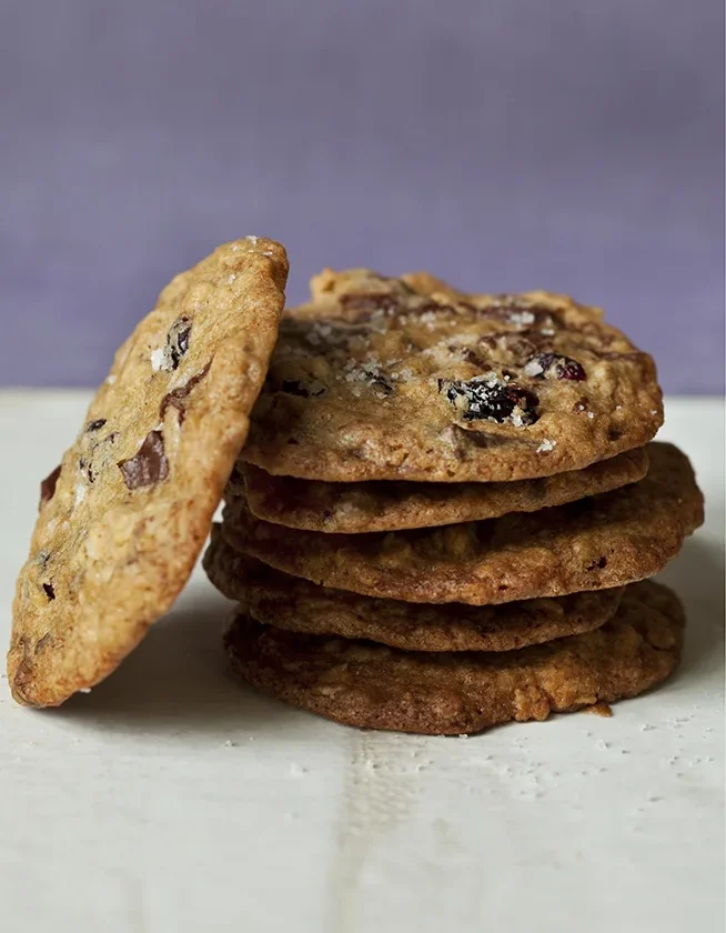 Stack of salty oatmeal chocolate chunk cookies with dried cranberries and flaky salt, with one cookie leaning on the side