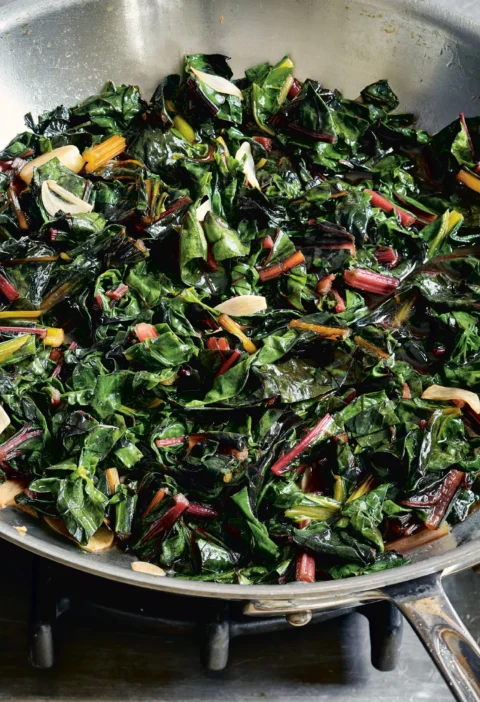 Ina Garten sautéed rainbow chard with colorful stems and garlic slices in a stainless steel sauté pan
