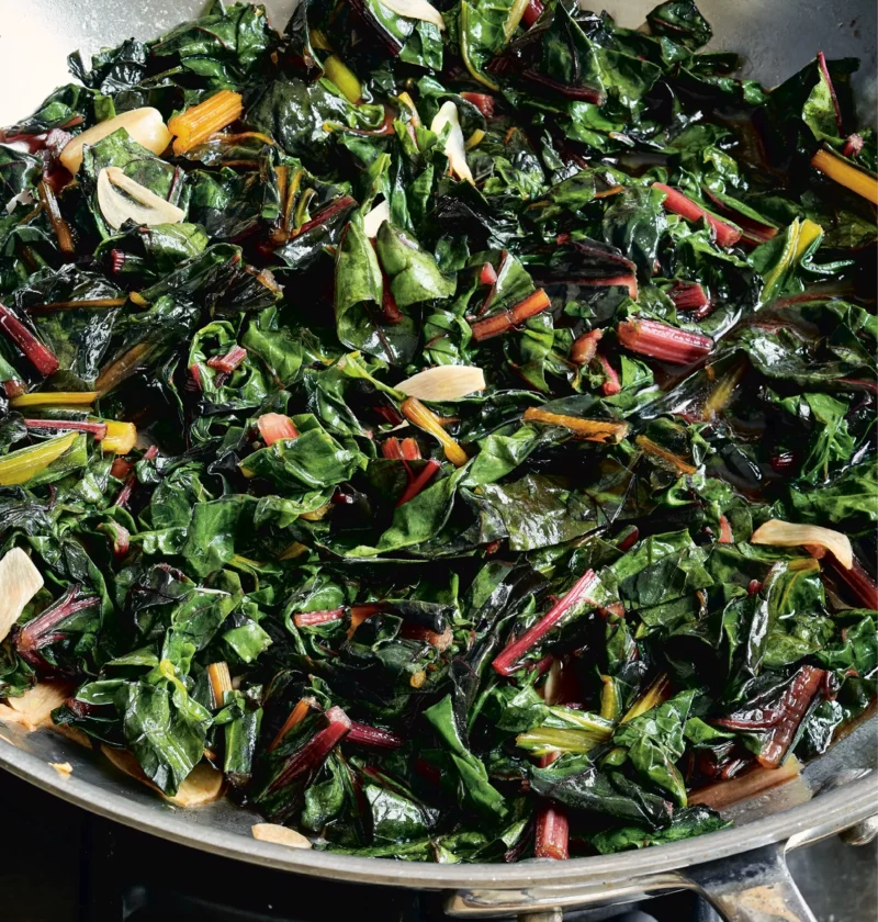 Ina Garten sautéed rainbow chard with colorful stems and garlic slices in a stainless steel sauté pan
