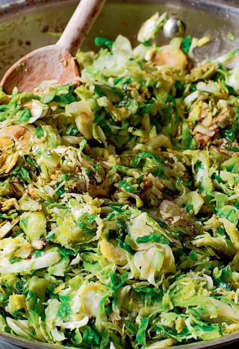 Ina Garten sautéed shredded brussels sprouts in a large sauté pan with a wooden spoon