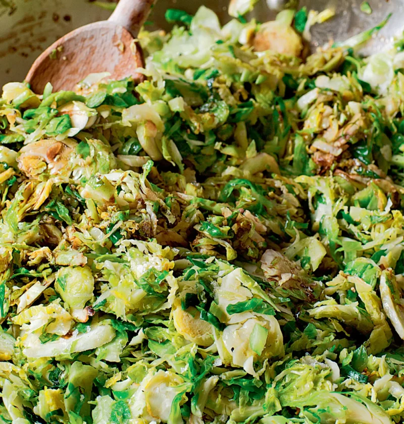 Ina Garten sautéed shredded brussels sprouts in a large sauté pan with a wooden spoon