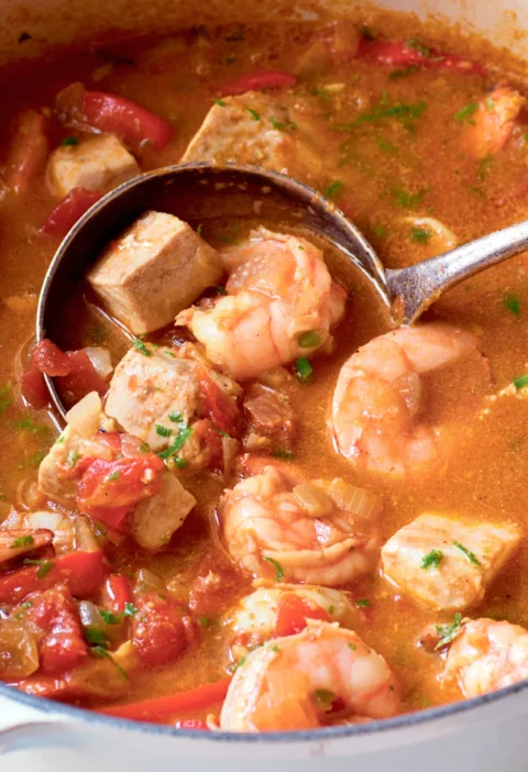 Ina Garten shrimp and swordfish curry in a white Dutch oven with shrimp, swordfish chunks and red pepper in a tomato curry broth