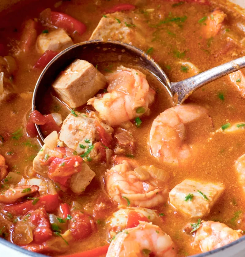 Ina Garten shrimp and swordfish curry in a white Dutch oven with shrimp, swordfish chunks and red pepper in a tomato curry broth