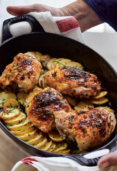 Ina Garten skillet-roasted chicken and potatoes with golden chicken thighs on sliced potatoes in a black cast-iron skillet