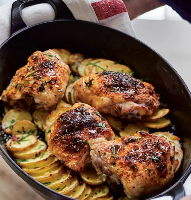 Ina Garten skillet-roasted chicken and potatoes with golden chicken thighs on sliced potatoes in a black cast-iron skillet