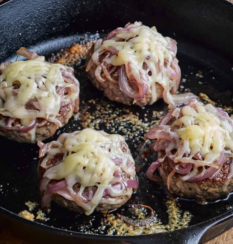 Ina Garten smashed hamburgers with caramelized onions and melted Gruyère cooking in a cast-iron skillet