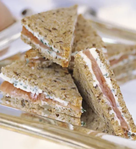 Ina Garten smoked salmon tea sandwiches cut into triangles with herb butter on seven-grain bread on a silver tray