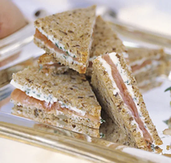 Ina Garten smoked salmon tea sandwiches cut into triangles with herb butter on seven-grain bread on a silver tray