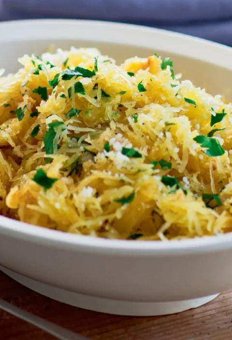 Ina Garten spaghetti squash with garlic and parmesan in a white bowl, topped with chopped parsley