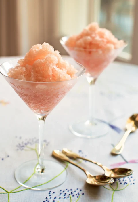 Ina Garten sparkling grapefruit granita piled in two stemmed martini glasses on an embroidered tablecloth with gold spoons