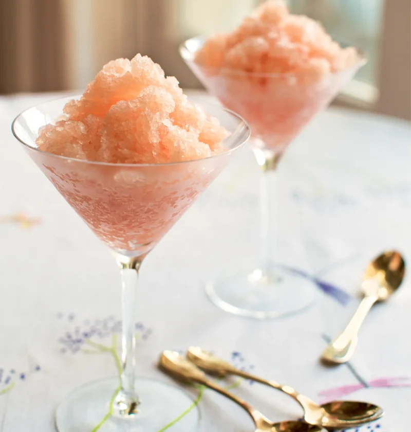 Ina Garten sparkling grapefruit granita piled in two stemmed martini glasses on an embroidered tablecloth with gold spoons