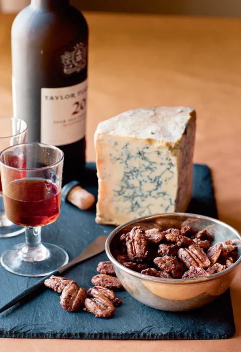 Ina Garten spiced pecans in a silver bowl beside blue cheese and a glass of port on a slate board