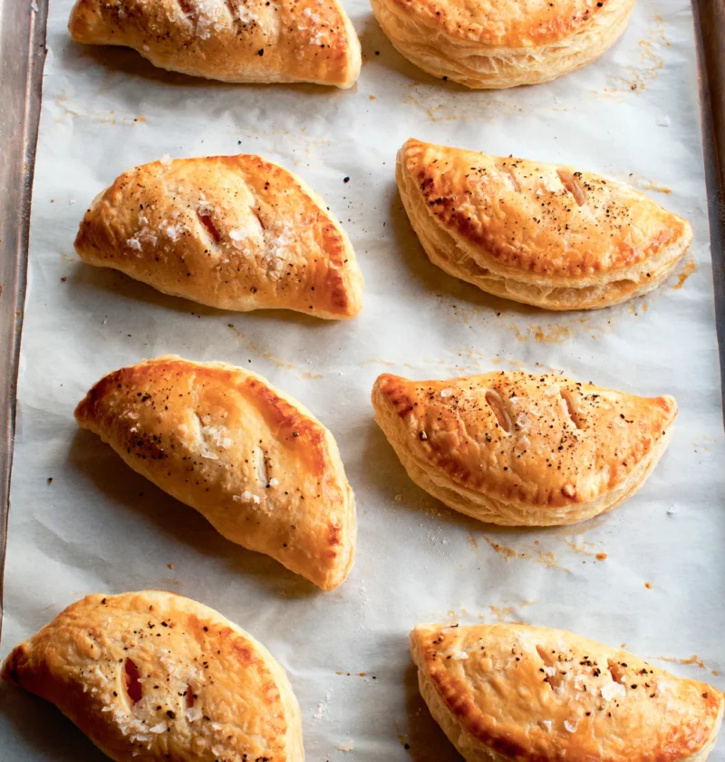 Ina Garten spicy sweet potato empanadas, golden puff pastry half circles sprinkled with flaked sea salt on a parchment-lined sheet pan