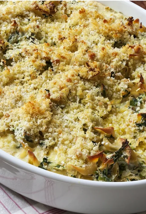 Ina Garten spinach and ricotta noodle pudding with a golden panko crust in a white oval baking dish