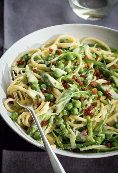 Ina Garten spring green spaghetti carbonara with peas, snow peas, asparagus and pancetta in a white bowl with a fork