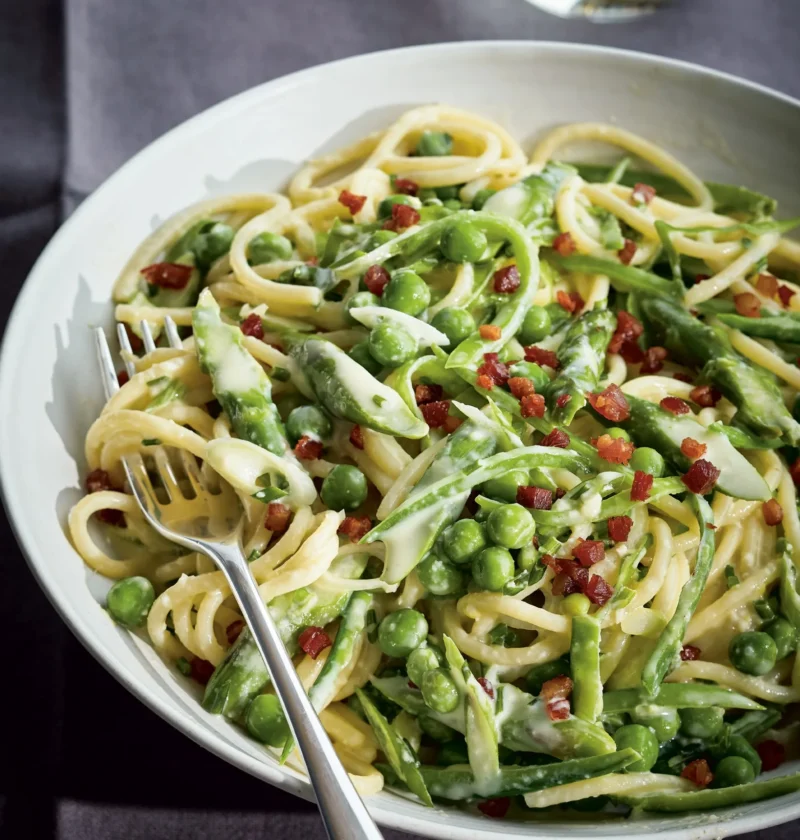 Ina Garten spring green spaghetti carbonara with peas, snow peas, asparagus and pancetta in a white bowl with a fork