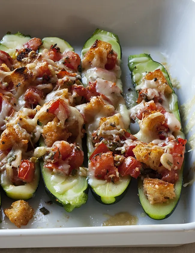 Ina Garten stuffed zucchini halves topped with sourdough croutons, diced tomatoes and melted Gruyère in a white baking dish